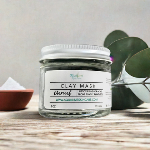 Aqualime Charcoal Clay Mask in a 2 oz glass bottle, surrounded by a fresh green leaf, highlighting the natural ingredients for clear and rejuvenated skin