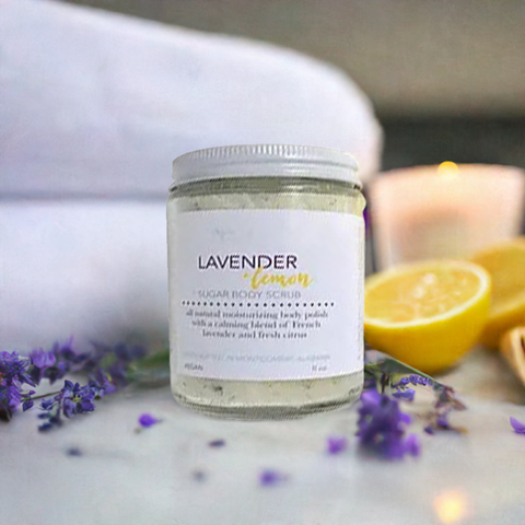 Aqualime Coffee Glow Shimmering Sugar Body Scrub in a glass bottle, surrounded by fresh green leaf, cinnamon sticks, and cut lemon, highlighting its aromatic and refreshing formula