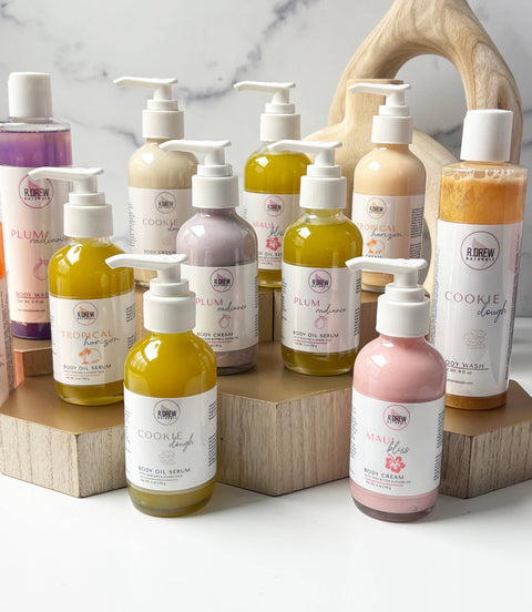 Multiple bottles of R. Drew Cookie Dough Shea Butter Body Cream placed on a cutting wooden plate, providing deep moisture and a soothing cookie dough scent