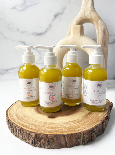 R. Drew Plum Radiance Body Oil Serum, 4 bottles placed on a wooden plate with a fresh background, offering deep hydration and a luxurious scent