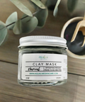 Aqualime Charcoal Clay Mask in a 2 oz glass bottle, accompanied by a bowl of activated charcoal and a fresh green leaf, highlighting the natural ingredients for detoxifying skin