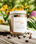 Aqualime Coffee Glow Shimmering Sugar Body Scrub in a glass bottle placed on a wooden surface, surrounded by coffee seeds, with a background of green leaves, yellow and pink flowers, highlighting its natural ingredients for glowing skin