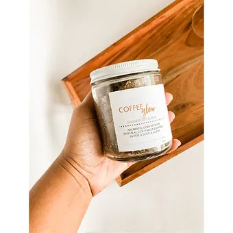 Aqualime Coffee Glow Shimmering Sugar Body Scrub in a glass bottle held in hand, placed inside a wooden box, showcasing the luxurious scrub with its natural ingredients for glowing skin