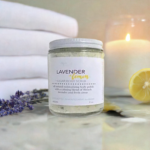 Aqualime Coffee Glow Shimmering Sugar Body Scrub in a glass bottle placed on white fabric, surrounded by fresh towel, cut lemon, leaves, and a glass candle for a calming ambiance