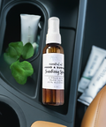 Aqualime Hand and Surface Sanitizing Spray placed on a car's plastic tray, accompanied by a fresh aloe vera leaf. The 2 oz amber spray bottle stands out, highlighting its compact design and practical use for on-the-go sanitizing