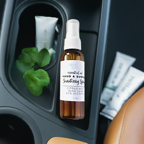 Aqualime Hand and Surface Sanitizing Spray placed on a car's plastic tray, accompanied by a fresh aloe vera leaf. The 2 oz amber spray bottle stands out, highlighting its compact design and practical use for on-the-go sanitizing