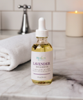 Aqualime Lavender Bath and Body Oil bottle placed on a white bathroom countertop with a soft towel, emphasizing its soothing, hydrating properties