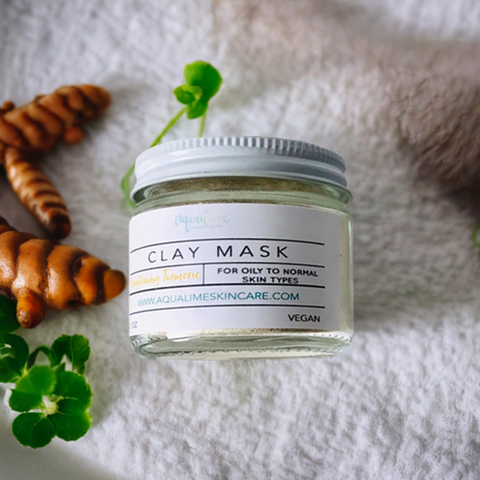 Aqualime Turmeric and Clay Facial Mask bottle placed on a white towel with turmeric roots and fresh green leaves, highlighting its brightening and soothing properties