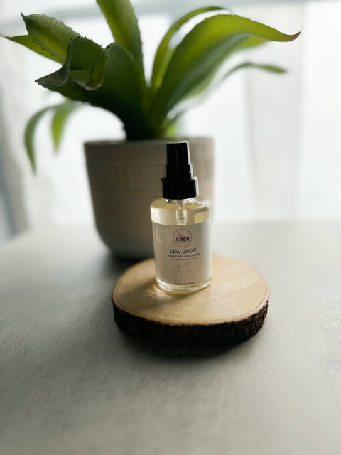 R. Drew Dew Drops Hyaluronic Acid Serum bottle on a wooden plate with an aloe vera pot, offering hydration and soothing benefits for all skin types