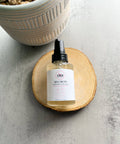 R. Drew Dew Drops Hyaluronic Acid Serum bottle placed on a cutting wooden plate with a pot on a floral background, enhancing hydration and soothing