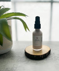 R. Drew Pink Clay + Calendula Super Fruit Facial Lotion bottle on cutting wooden plate with aloe plant pot, featuring antioxidant-rich skin renewal ingredients