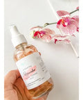 R. Drew Rosewater Toning Mist bottle held in hand with rose leaves surrounding it, designed to balance skin and reduce redness