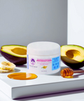 Reagan Sanai Avocado & Banana Deep Conditioner bottle placed on white background table with half-cut avocado, banana, and honey for nourishing and moisturizing hair