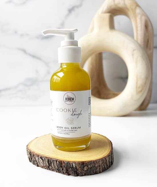 R. Drew Cookie Dough Body Oil Serum bottle placed on cutting wooden plate with fresh background, offering deep hydration and soothing cookie dough scent