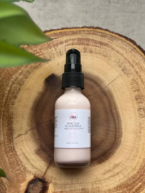 R. Drew Pink Clay + Calendula Super Fruit Facial Lotion bottle on a cutting wooden plate, featuring antioxidant-rich ingredients for skin renewal and protection