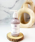 R. Drew Plum Radiance Shea Butter Body Cream bottle placed on a wooden plate with a fresh background, offering deep hydration and a delightful fragrance